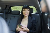 Empresária usando seu celular no banco de trás de um carro — Fotografia de Stock