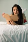 Chinês mulher em sua cama lendo um livro — Fotografia de Stock