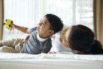 Азиатская мать и сын играют с игрушками на кровати — стоковое фото