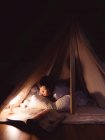 Милая маленькая девочка читает книгу в палатке — стоковое фото