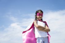 Young little cute asian girl posing in superhero costume against blue sky — Stock Photo