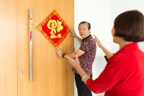 Old asian couple decorating door for chinese new year — Stock Photo