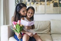 Молода азіатська мати з милою дочкою обіймається вдома з квітами і шаблоном — стокове фото