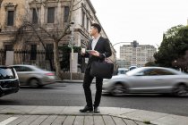 Hombre de negocios chino parado al aire libre sosteniendo una taza de café y una tableta, España - foto de stock