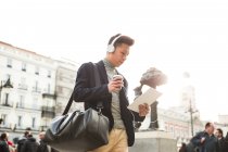 Casual jovem chinês com um computador tablet. fones de ouvido e uma xícara de café na Puerta del Sol, Madrid, Espanha — Fotografia de Stock