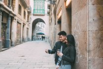 Joven pareja asiática tomando café en la calle y mirando el teléfono móvil - foto de stock