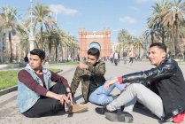 Indian friends tourist drinking beer seated on the ground in Arc of triump Barcelona Spain — Stock Photo