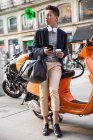 Lässiger junger Chinese mit Smartphone. auf einem motorrad sitzend an der puerta del sol, madrid, spanien — Stockfoto