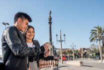 Молодая пара туристов смотрит мобильный телефон у памятника Колумбу — стоковое фото