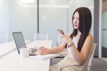 Junge Frau macht sich in modernem Büro Notizen mit Handy in der Hand — Stockfoto