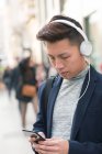 Casual young chinese man using phone and headphones in the street, Spain — Stock Photo