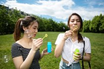 Niedliche asiatische Freundinnen machen Seifenblasen im Park. — Stockfoto