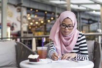 Mujer joven anotando algo de información en un café - foto de stock