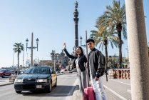 Young tourist couple waving a taxi on the street in barcelona, spain — Stock Photo