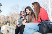 Philippine friends women sharing the screen of an electronic tablet in Retiro Park Madrid next to the lake, Spain — Stock Photo