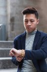 Casual jovem chinês homem verificando o tempo olhando para o seu relógio na rua, Espanha — Fotografia de Stock