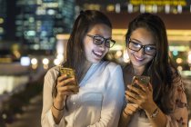 Две молодые девушки со своими смартфонами в городе — стоковое фото