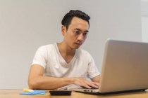 Hombre joven que trabaja con su ordenador portátil en el entorno de inicio - foto de stock