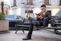Homme d'affaires chinois lisant dans la rue et assis sur un banc — Photo de stock