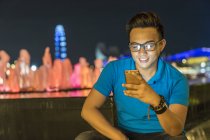 Молодой человек играет со своим смартфоном в городе — стоковое фото
