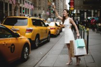 Mujer joven llamando a un taxi amarillo en la ciudad después de sus grandes compras . - foto de stock