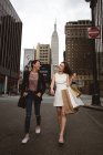 Zwei schöne elegante Frauen, die an der Straße vorbeigehen und Einkaufstüten mit Empire-Staat im Rücken halten. — Stockfoto