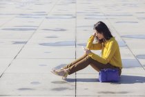 Вид збоку весела молода китайська жінка сидить на підлозі зі смартфоном — стокове фото