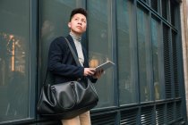 Lässiger junger chinesischer Mann schaut weg und hält einen Tablet-Computer in madrid, spanien — Stockfoto