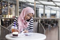 Mujer joven anotando algo de información en un café - foto de stock
