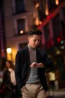 Lässiger junger chinesischer Mann, der nachts auf der Straße auf seine Uhr schaut, Spanien — Stockfoto