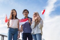 Um grupo de amigos posando com as bandeiras de Singapura. — Fotografia de Stock