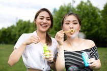 Cute asian girlfriends making soap bubbles in the park. — Stock Photo