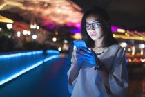 Jeune dame utilisant son téléphone portable dans la rue, fond de lumière de nuit — Photo de stock