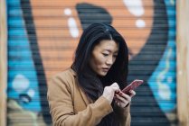 Mujer china revisando su teléfono en Madrid mirando al móvil, España - foto de stock