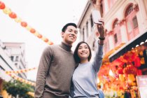 Feliz asiático pareja celebrando chino año nuevo en ciudad y tomando selfie - foto de stock