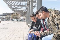Amigos indios turistas esperando en una estación de metro de Barcelona para el tren con teléfono móvil y riendo - foto de stock