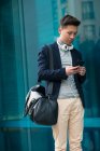 Casual young chinese man using phone and headphones in the street, Spain — Stock Photo