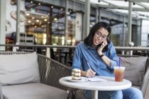 Mujer joven anotando algo de información en un café . - foto de stock