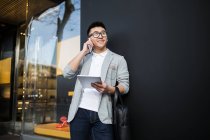 Веселый китайский бизнесмен разговаривает по телефону на улице и держит планшетный компьютер, Испания — стоковое фото