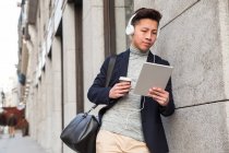 Casual young chinese man with a tablet ,headphones, and a cup of coffee in Madrid, Spain — Stock Photo