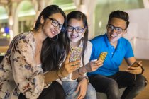 Молодые красивые азиатские друзья, использующие смартфоны на открытом воздухе — стоковое фото