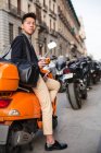 Lässiger junger Chinese mit Smartphone. auf einem motorrad sitzend an der puerta del sol, madrid, spanien — Stockfoto