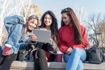 Philippine friends women enjoying with tablet and mobile phone in Retiro Park Madrid next to the lake. — Stock Photo