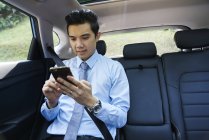 Jovem homem de negócios verificando móvel no carro — Fotografia de Stock