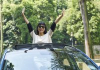 Young woman standing through the opening of a sun roof on a car — Stock Photo