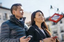 Asian Chinesse  honeymooners tourist walking around plaza de la opera and teatro real looking at their mobile phones in Madrid — Stock Photo