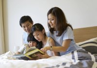 Famiglia che condivide un libro in camera da letto — Foto stock