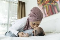 Asiatico musulmano madre baci bambino su letto — Foto stock