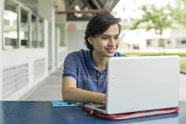 Estudiante malayo trabajando en el proyecto escolar en el ordenador portátil - foto de stock