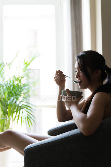 Chinese young woman having breakfast in the sofa i — Stock Photo